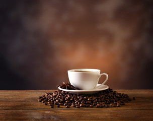 Cup of coffee with grains on wooden table on dark background