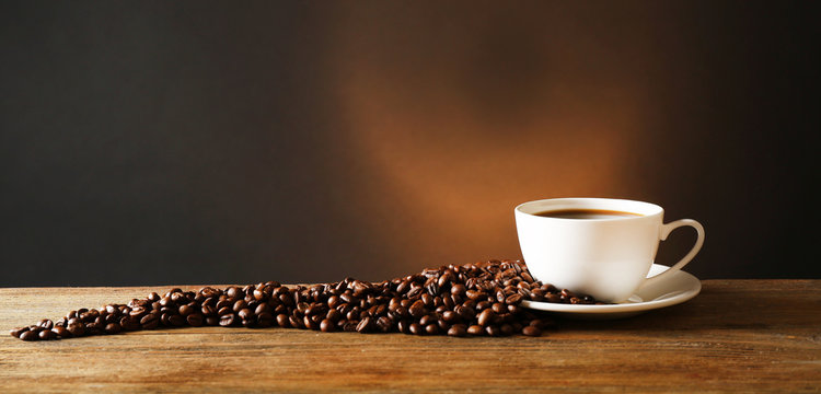 Fototapeta Cup of coffee with grains on wooden table on dark background