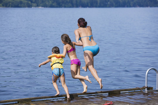 Mother and daughters jumping into lake