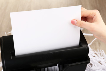 Female hand destroying sheet of paper with shredder on wooden table, closeup