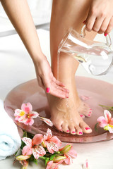 Woman washing beautiful legs in bowl, on light background. Spa procedure concept