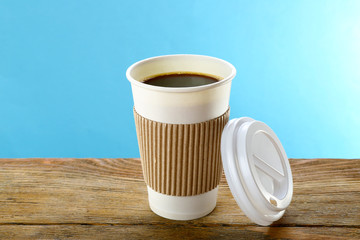 Paper cup of coffee on wooden table on blue background