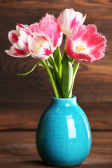 Beautiful tulips in vase on wooden background