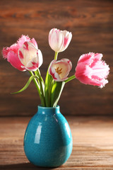 Pink tulips in vase on wooden background