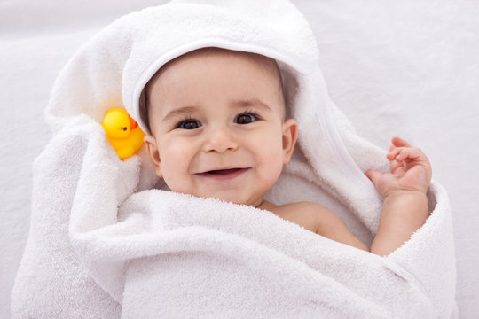 Adorable baby smiling wrapped in white towel with yellow duck