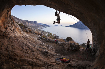 Young woman lead climbing in cave with beautiful view in background