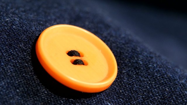 Sewing an orange button on jeans, denim, close up