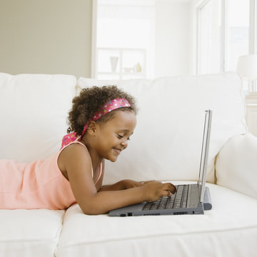 Mixed race girl typing on laptop in living room