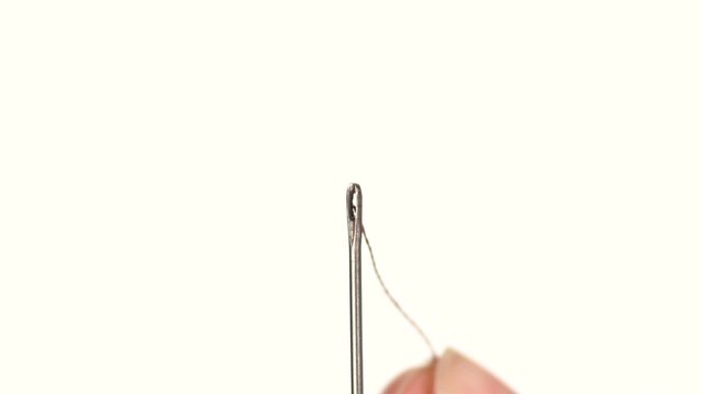 Light thread going through a needle hole on white background