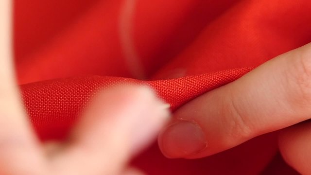 Woman sewing with needle, thread and thimble on red cloth, close