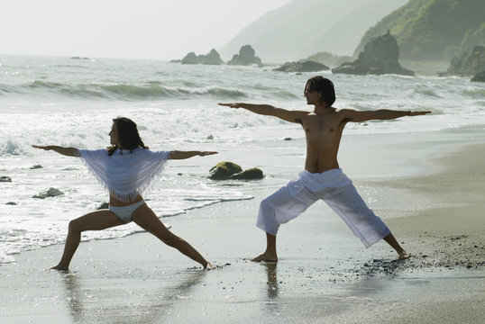 Hispanic couple doing yoga at beach