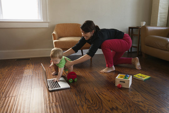 Caucasian mother keeping toddler son from laptop