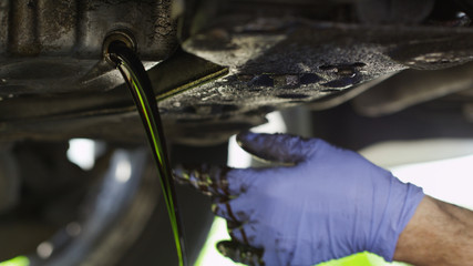 Mechanic draining oil from a car - obrazy, fototapety, plakaty