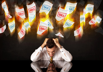 Obraz premium Depressed businessman sitting under burning tax and bill papers