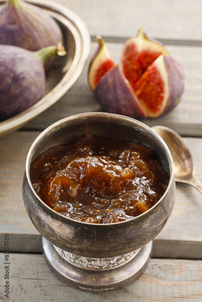 Sticker bowl of fig jam and raw figs on rustic wooden table