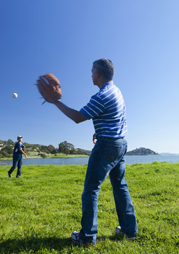 Hispanic Father And Son Playing Catch In Park