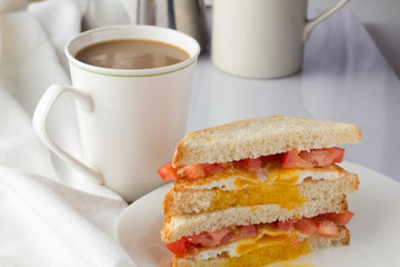 Sandwich with fried egg and tomatoes and cup of coffee