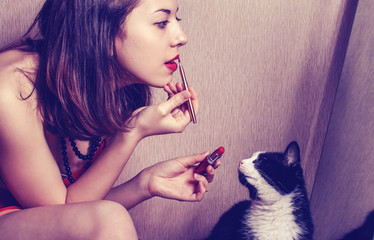 The girl paints lips with lipstick looking in the mirror