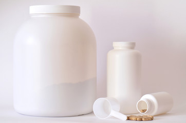 Fototapeta na wymiar Big jar of protein powder, bottles and scoop