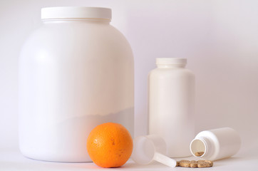 Fototapeta na wymiar Big jar of protein powder, bottle of pills, orange and scoop