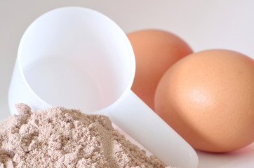 White scoop in heap of chocolate protein powder and eggs