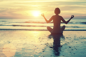 Female in yoga meditation pose at amazing sunset on the sea.