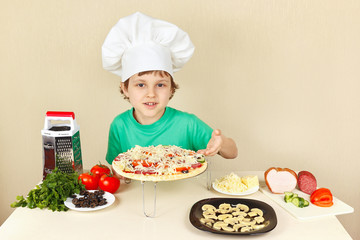 Little boy in chefs hat shows how to cook a pizza