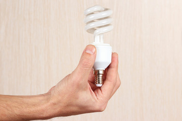 Hand holding spiral tungsten lightbulb on light wood background