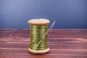 Vintage grunge wooden green thread spool with needle on wooden b