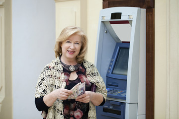 Mature blonde woman counting money near ATM