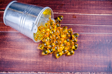 Fish oil from silver bucket with wooden texture background