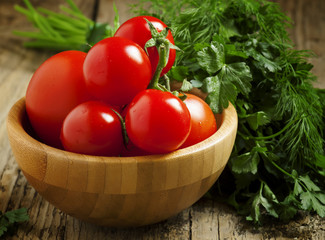 Fresh red tomatoes with parsley and dill on a wooden table