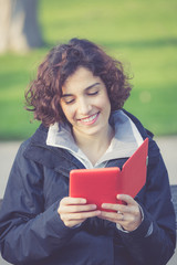 young girl sitting on a bench at park and reading E-book