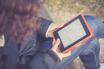 young girl sitting on a bench at park and reading E-book