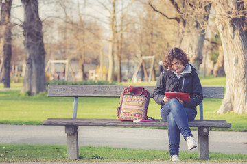 young girl sitting on a bench at park and reading book