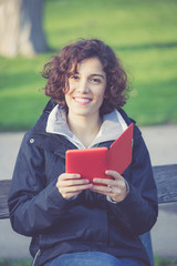 young girl sitting on a bench at park and reading E-book
