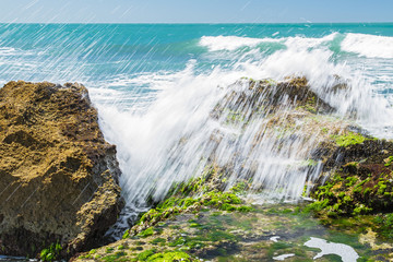 Turquoise rolling wave slamming on the rocks .