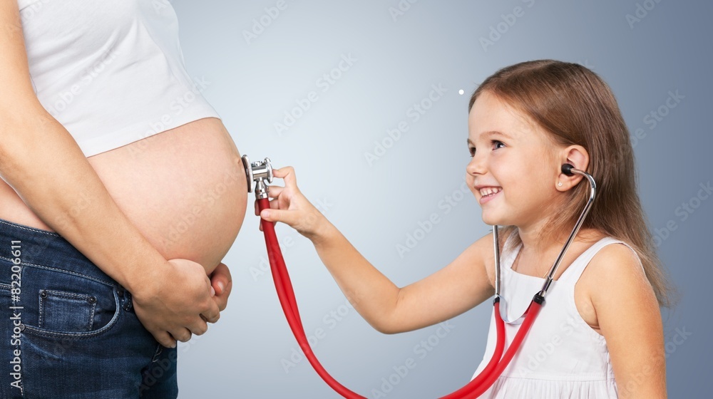 Wall mural Pregnant. Kid girl examining pregnant mother's tummy