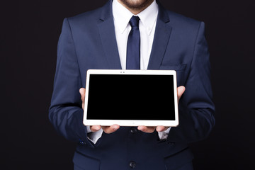 Businessman displaying a tablet computer against dark background