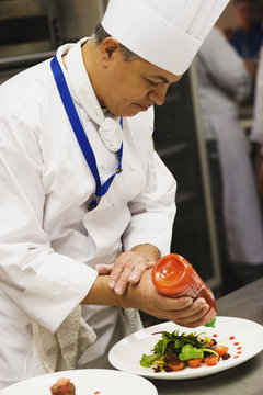 Hispanic male chef garnishing plate of food