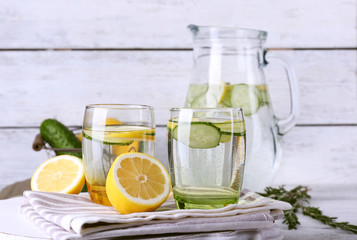 Fresh water with lemon and cucumber in glassware on wooden background