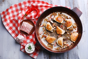 Fried dumplings with onion and bacon in frying pan, on wooden table background