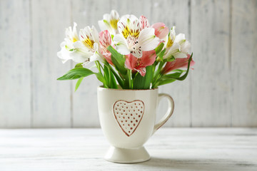 Beautiful flowers in cup, on wooden background