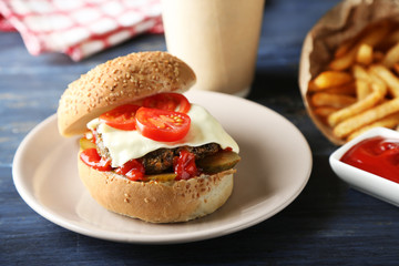 Tasty burger and french fries on plate, on wooden table background. Unhealthy food concept