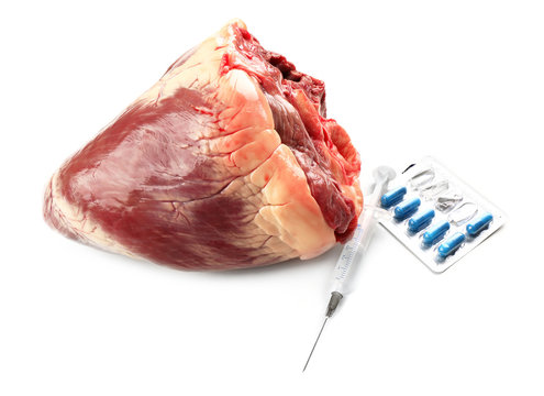 Raw animal heart with syringe and tablets isolated on white