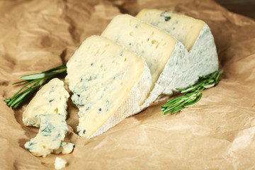 Pieces of tasty blue cheese with rosemary on paper background