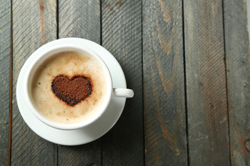 Cup of cappuccino with heart of cocoa on wooden table