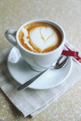 Cup of cappuccino with heart on foam on table in cafe