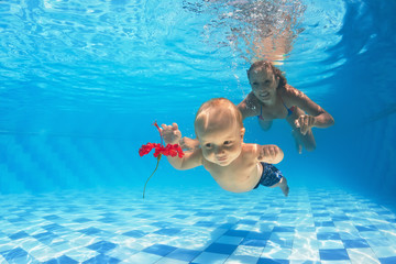 Child with woman diving for a red flower in pool