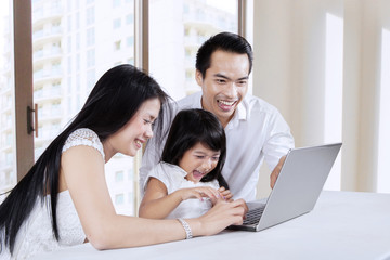 Fototapeta premium Two parents using laptop with daughter